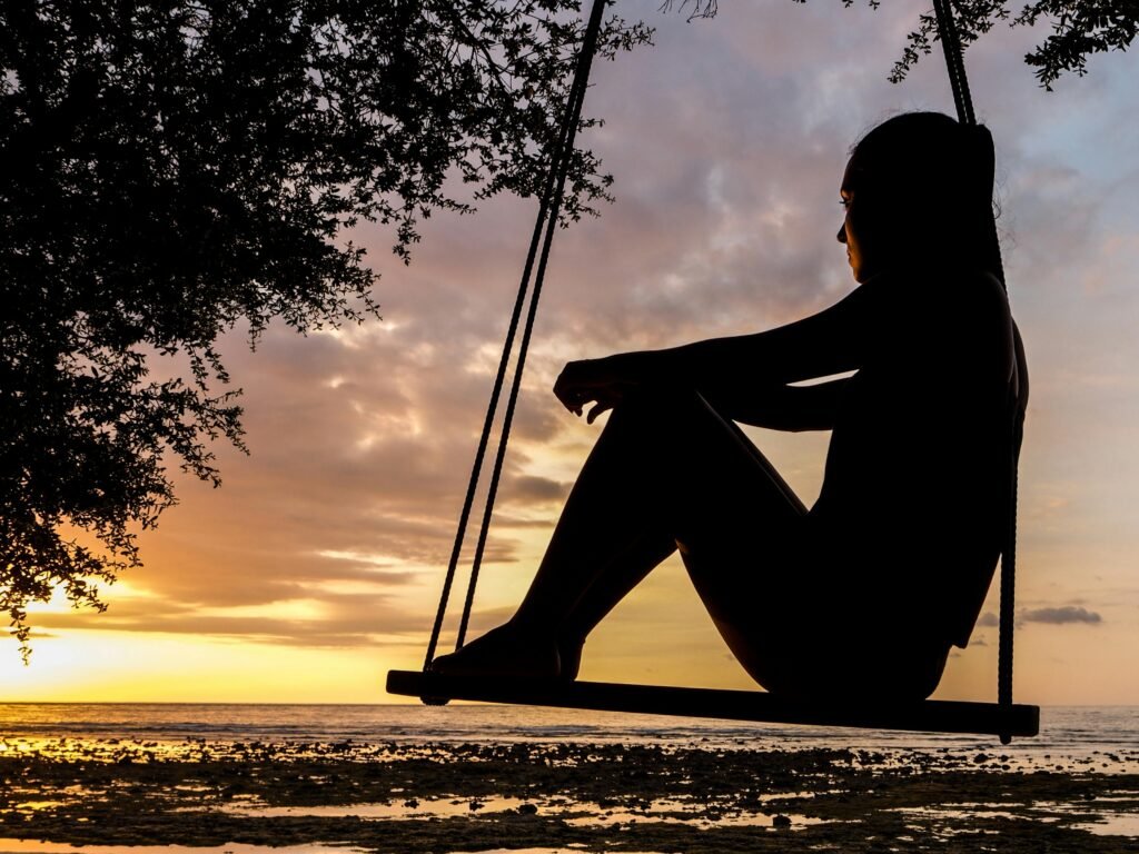 pexels-photo-289998-289998 A serene sunset silhouette of a woman sitting on a swing by the seashore, evoking tranquility and reflection.